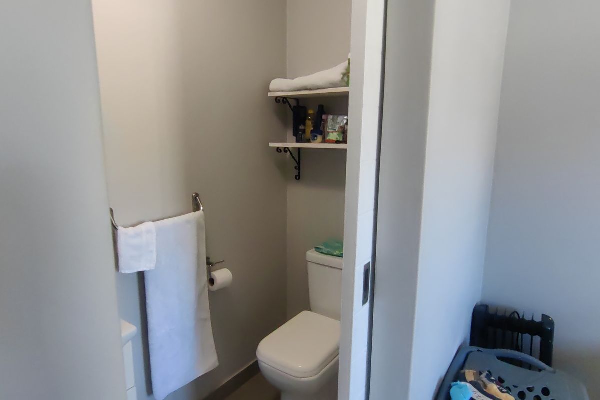 A compact bathroom featuring a toilet, wall-mounted shelving, and a towel rail, accessible via a sliding door.