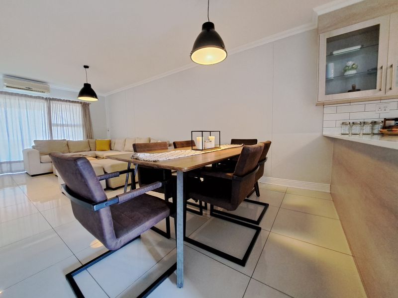 Spacious open-plan living and dining area featuring modern tiled floors, neutral walls, split-system air conditioning, and a well-appointed kitchen corner.