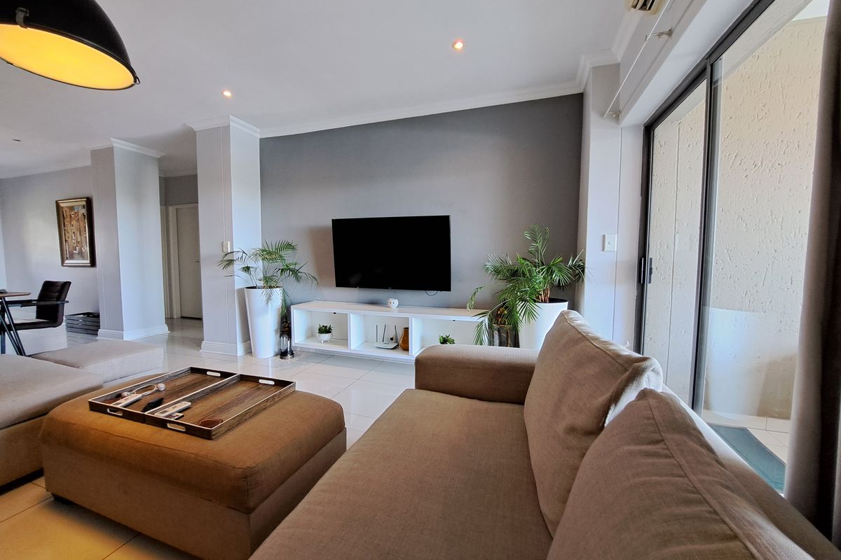 A bright and modern living room featuring tiled floors, recessed lighting, and large sliding glass doors that provide access to the balcony.