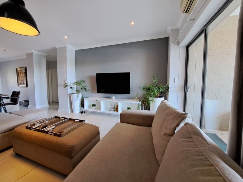 A bright and modern living room featuring tiled floors, recessed lighting, and large sliding glass doors that provide access to the balcony.