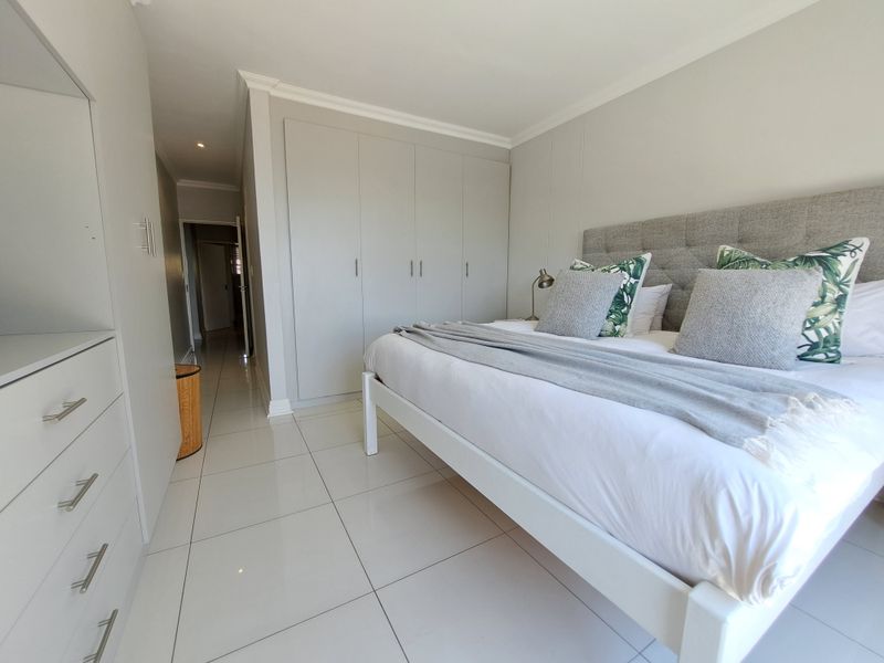 A well-maintained bedroom featuring neutral wall tones, large-format floor tiles, and extensive built-in cupboard storage.