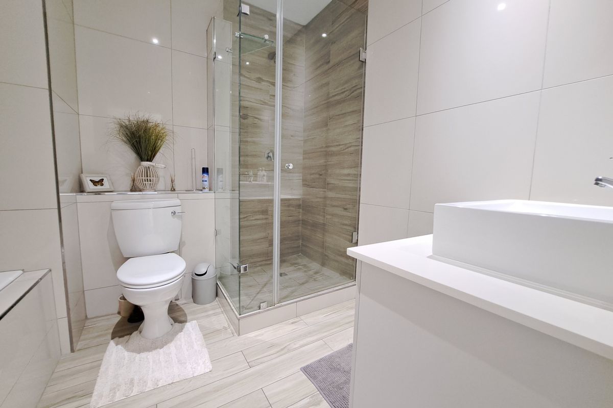 A modern, well-maintained bathroom featuring a glass-enclosed shower, contemporary vessel sink, vanity cabinet, and neutral floor-to-ceiling tiling.