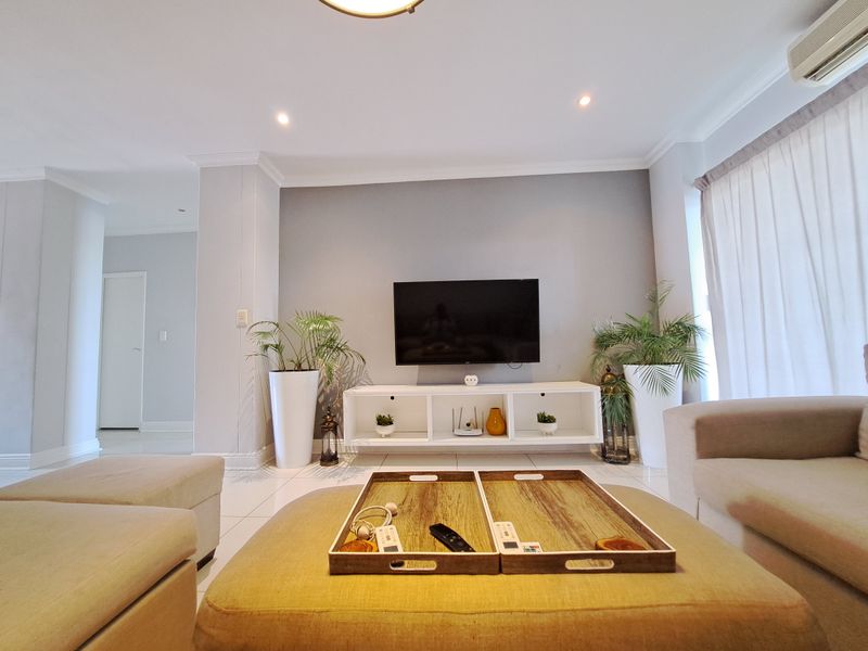 A well-maintained living room featuring tiled flooring, recessed downlighting, and a wall-mounted air conditioning unit, creating a bright and comfortable living space.