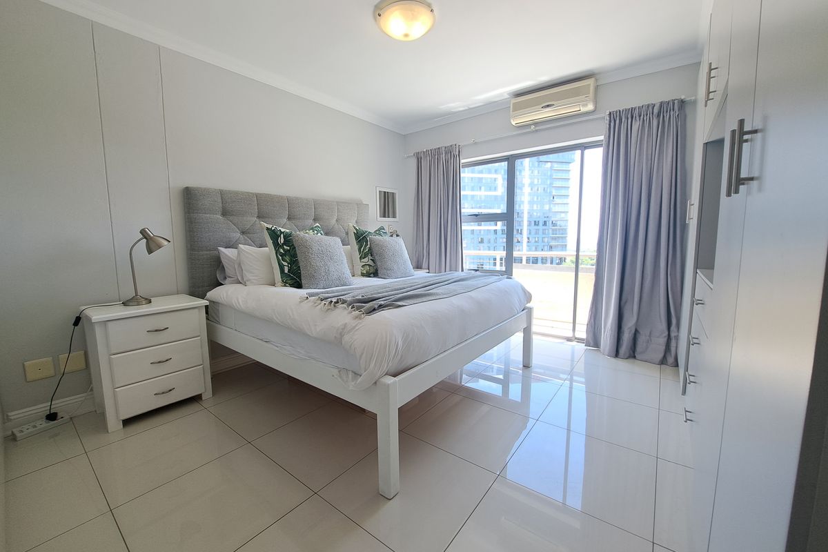 A well-maintained bedroom featuring tiled flooring, built-in cupboards, an air conditioning unit, and a sliding glass door providing natural light.