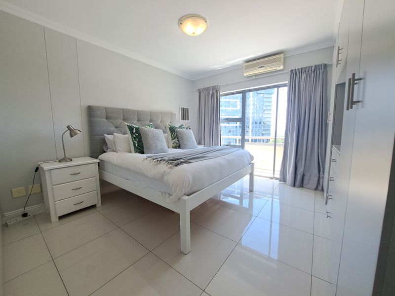 A well-maintained bedroom featuring tiled flooring, built-in cupboards, an air conditioning unit, and a sliding glass door providing natural light.