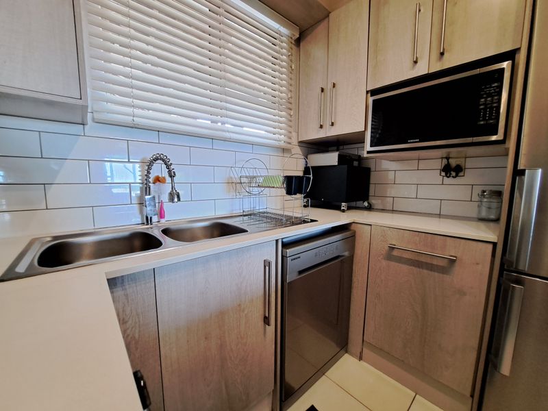 Modern kitchen featuring light wood-tone cabinetry, subway tile backsplash, integrated dishwasher, built-in microwave, and a double stainless steel sink with gooseneck faucet.