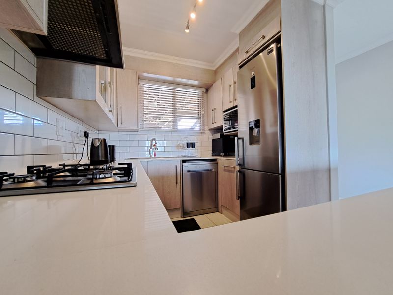 Modern kitchen featuring light wood cabinetry, quartz countertops, subway tile backsplash, and integrated stainless steel appliances including a gas hob and dishwasher.
