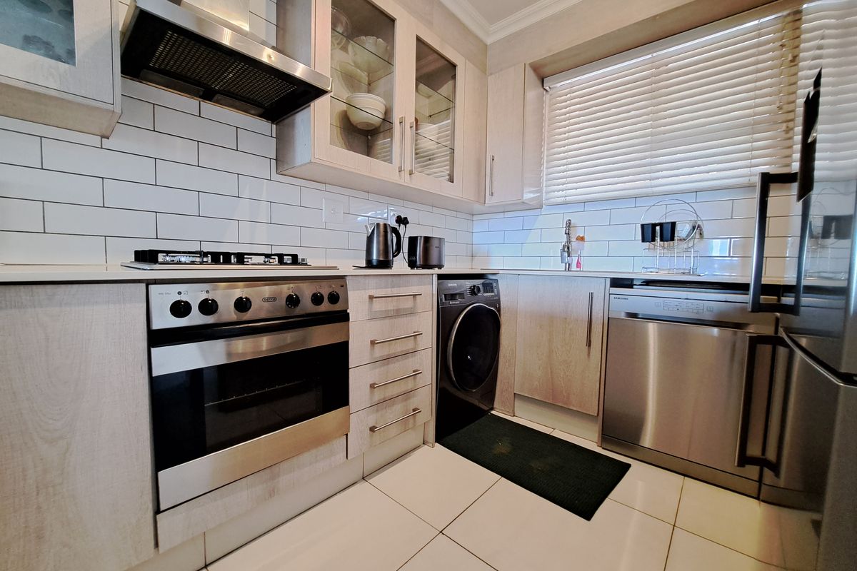 Modern kitchen featuring light wood cabinetry, subway tile backsplash, stainless steel appliances including a gas hob, oven, dishwasher, and built-in washing machine.