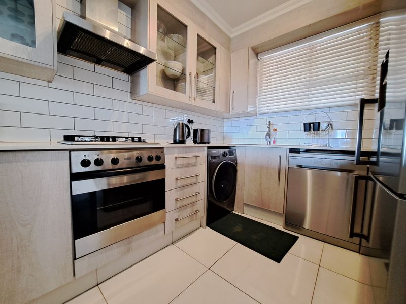 Modern kitchen featuring light wood cabinetry, subway tile backsplash, stainless steel appliances including a gas hob, oven, dishwasher, and built-in washing machine.
