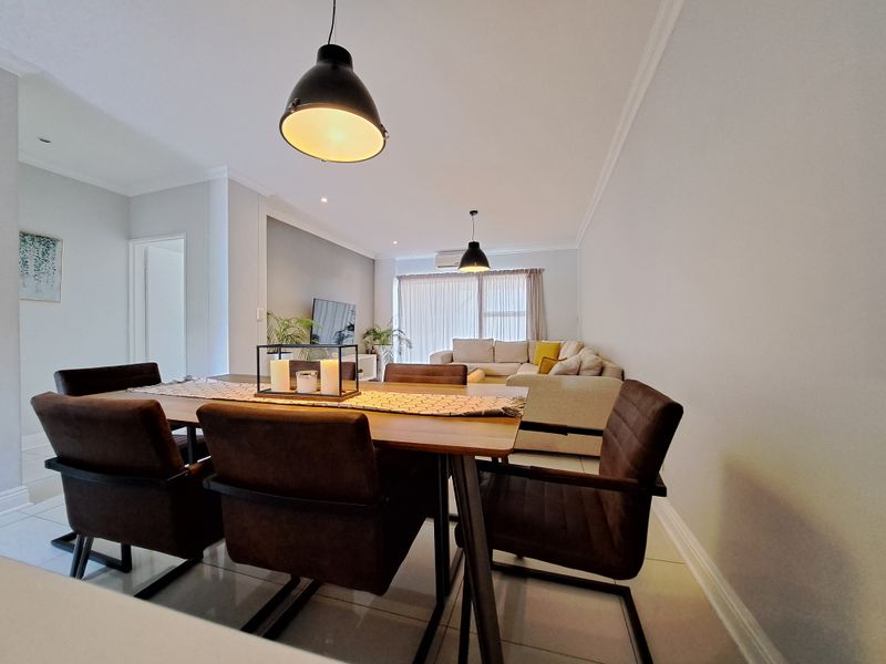 A bright open-plan living and dining area featuring tiled floors, modern pendant lighting, and an integrated air conditioning unit.