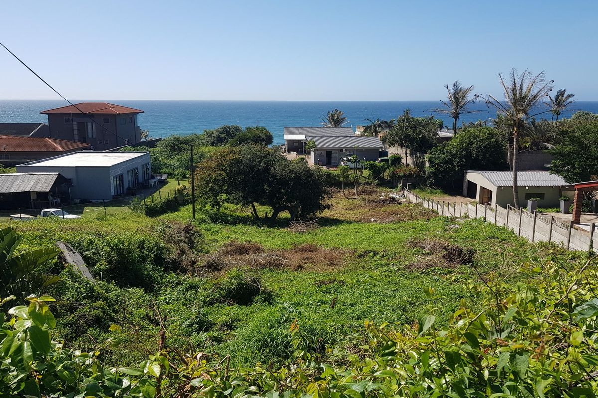 A vacant residential plot featuring coastal views, surrounded by established neighborhood properties and mature vegetation.