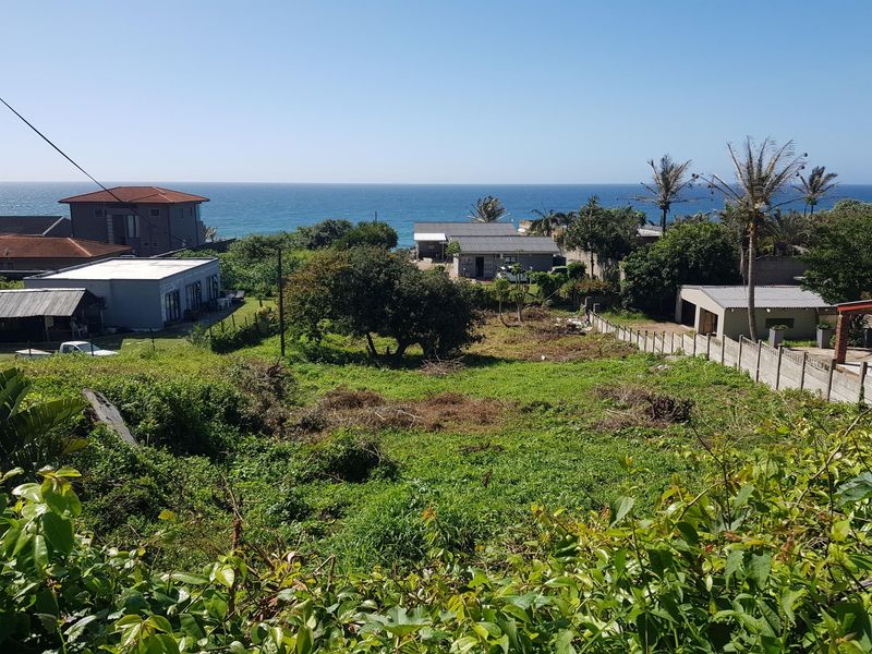 A vacant residential plot featuring coastal views, surrounded by established neighborhood properties and mature vegetation.