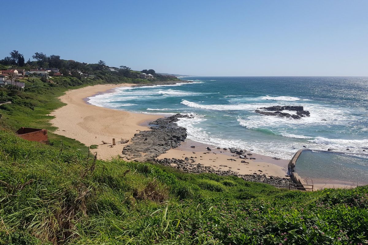 A scenic coastal view overlooking a sandy beach, rocky shoreline, and a tidal pool, showcasing the natural landscape of the residential area.