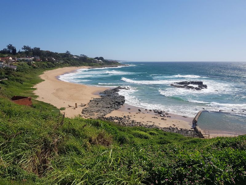 A scenic coastal view overlooking a sandy beach, rocky shoreline, and a tidal pool, showcasing the natural landscape of the residential area.