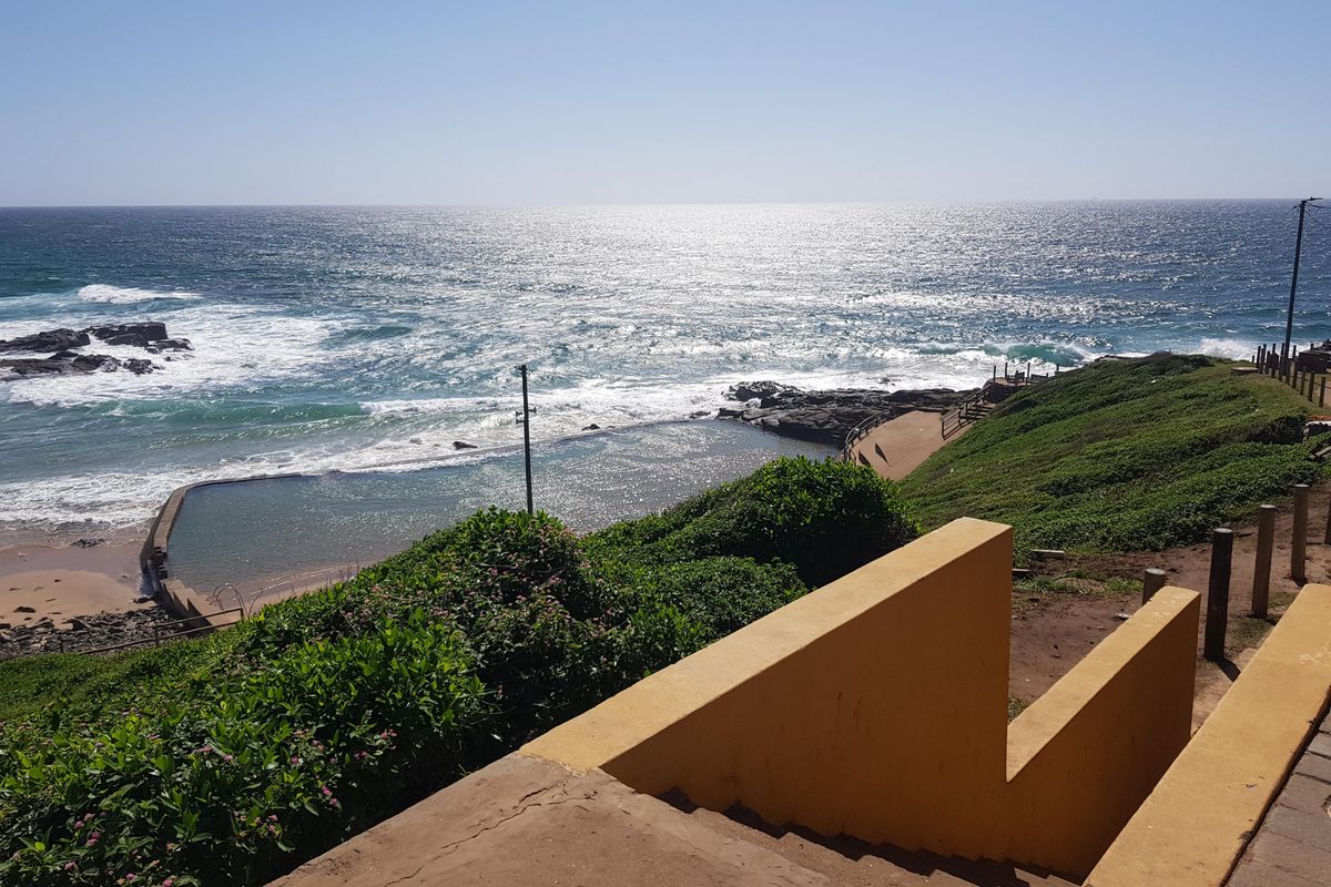 A scenic view overlooking a coastal tidal pool and the ocean, featuring a concrete staircase leading down towards the shoreline.
