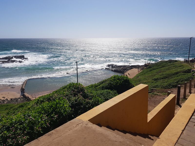 A scenic view overlooking a coastal tidal pool and the ocean, featuring a concrete staircase leading down towards the shoreline.