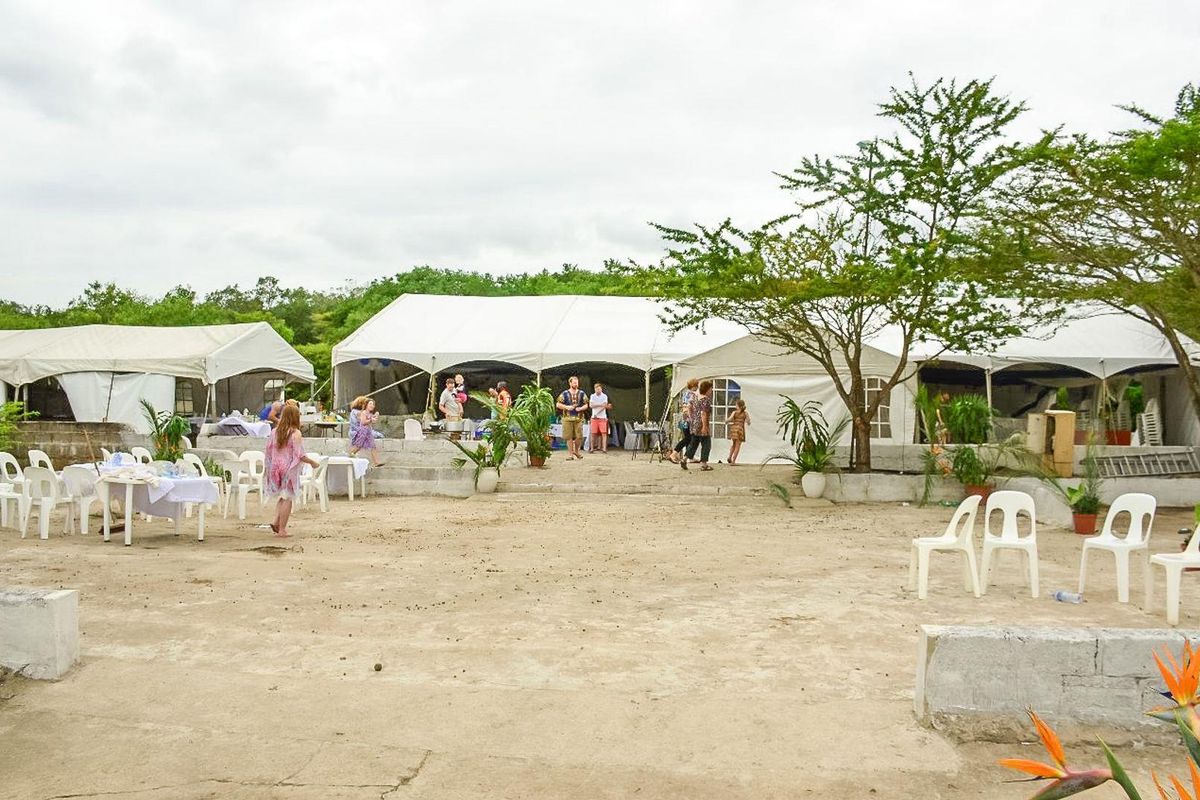 Outdoor event space featuring large temporary marquee tents set on an unpaved, open-air ground area with concrete retaining wall borders.