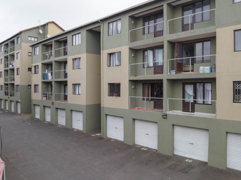 Exterior view of a multi-story apartment complex featuring ground-level roller garage doors and upper-level balconies with steel balustrades.