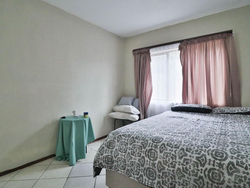 A functional bedroom featuring tiled flooring and a window with an installed curtain rod.