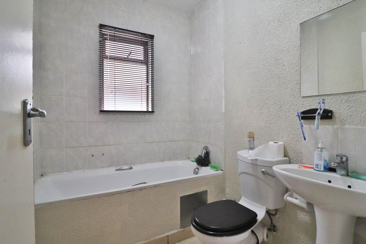 A functional bathroom featuring a bathtub, pedestal basin, and toilet, with tiled splashbacks and a window for natural light.