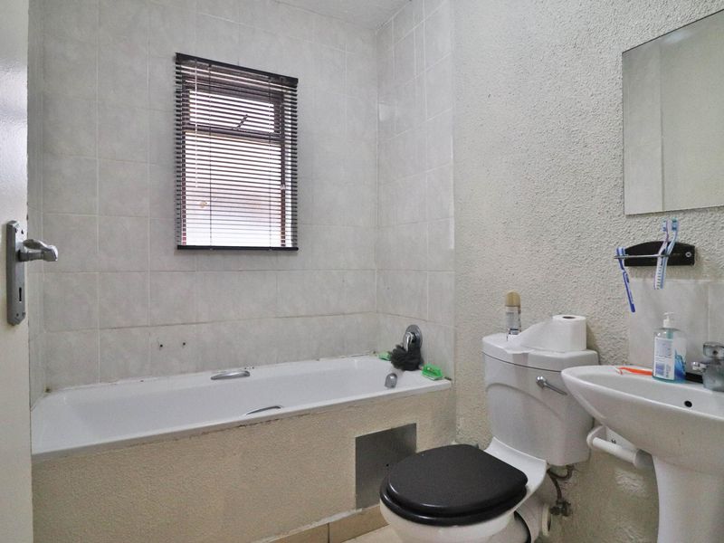 A functional bathroom featuring a bathtub, pedestal basin, and toilet, with tiled splashbacks and a window for natural light.