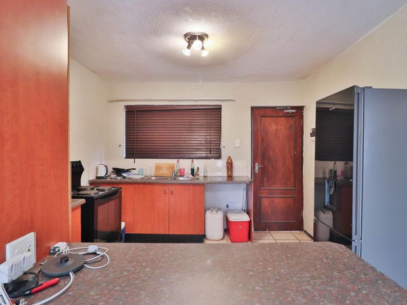 A functional kitchen featuring laminate cabinetry, laminate countertops, a stainless steel sink, and an electric stove, with direct access to an exterior door.