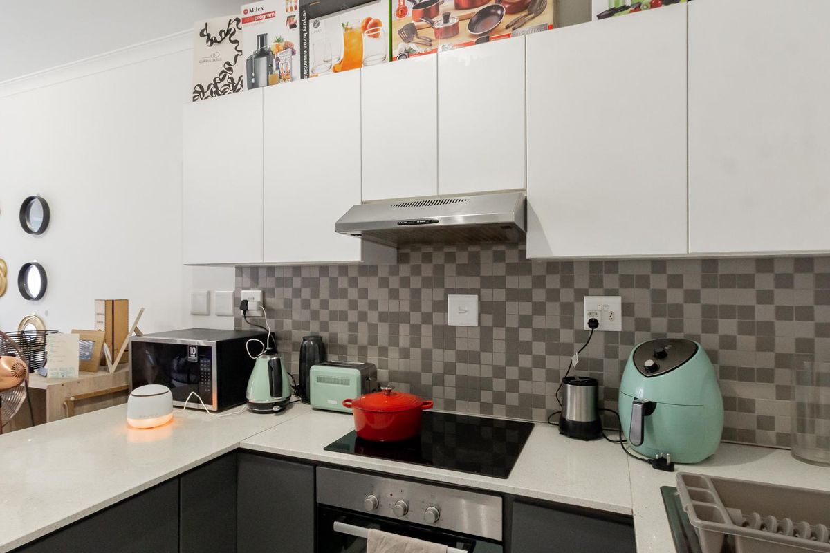A modern kitchen featuring contrasting white upper and dark lower cabinetry, stone countertops, and a mosaic tile backsplash with integrated stainless steel appliances.