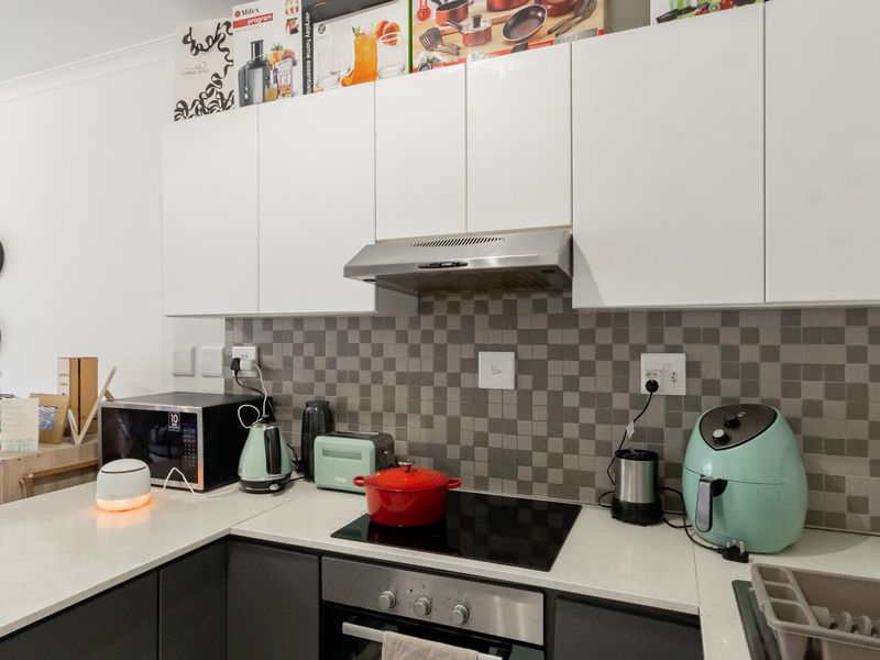 A modern kitchen featuring contrasting white upper and dark lower cabinetry, stone countertops, and a mosaic tile backsplash with integrated stainless steel appliances.