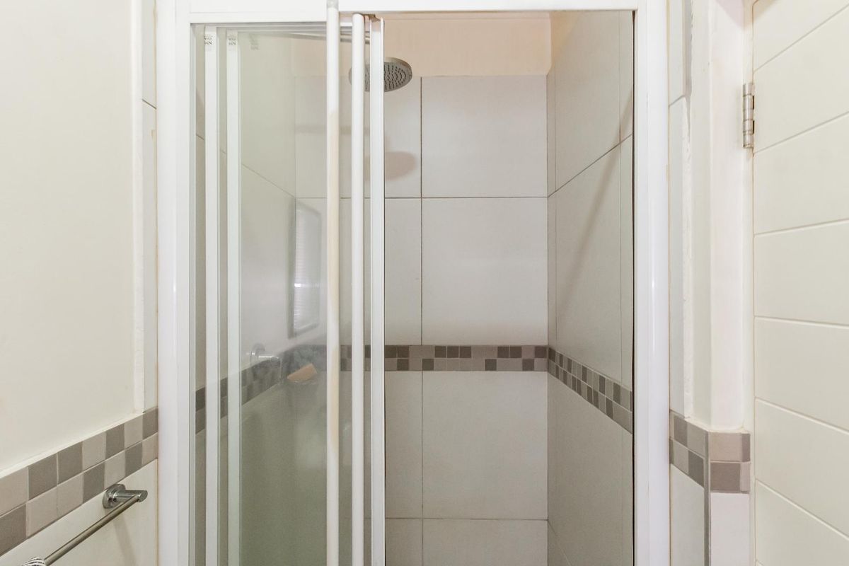 A clean bathroom shower stall featuring white wall tiles with a decorative mosaic border and a modern shower head.