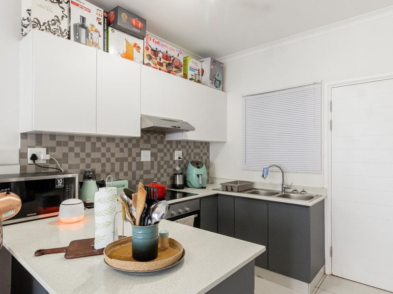Modern kitchen featuring two-tone cabinetry, stone countertops, integrated appliances, and a tiled splashback, offering a functional and contemporary cooking space.