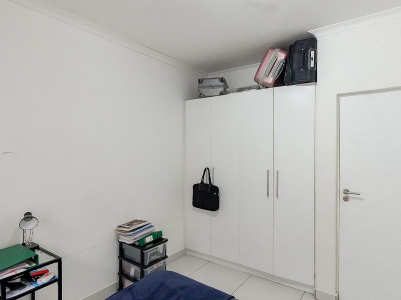 A bedroom featuring white tiled flooring, a built-in wardrobe with ample storage, and neutral wall finishes.