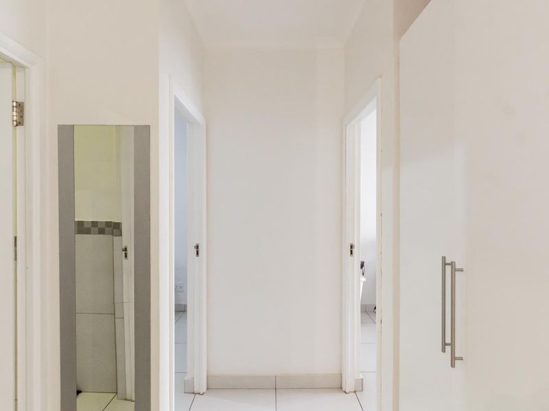 A clean, neutral hallway featuring tiled flooring and built-in storage cupboards, providing access to multiple rooms within the apartment.