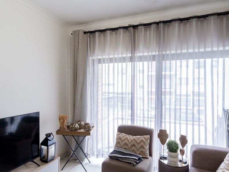 A bright living room featuring large sliding glass doors with floor-to-ceiling curtains and neutral tiled flooring.