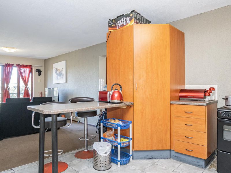 Open plan living area featuring a compact kitchen with built-in cabinetry, laminate countertops, and a freestanding stove, leading to a balcony with sliding doors.