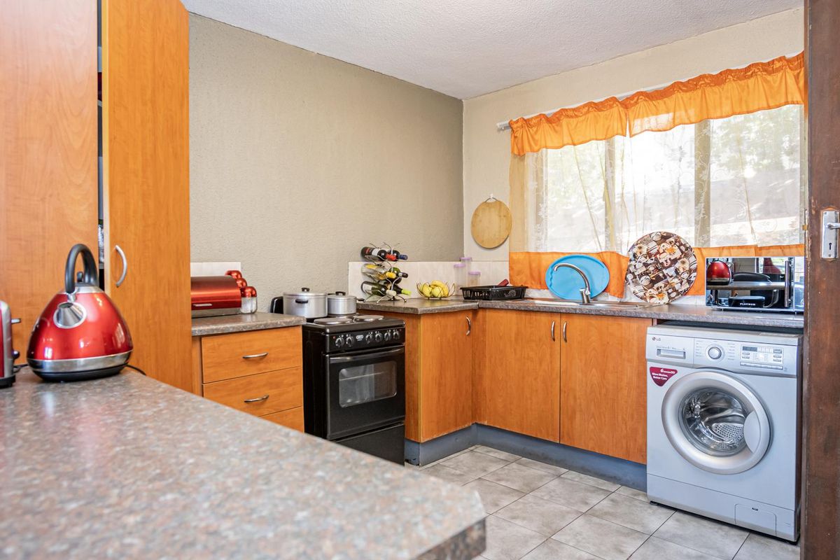 A functional kitchen featuring wood-look cabinetry, laminate countertops, a freestanding stove, and a dedicated space for a washing machine with tiled flooring.