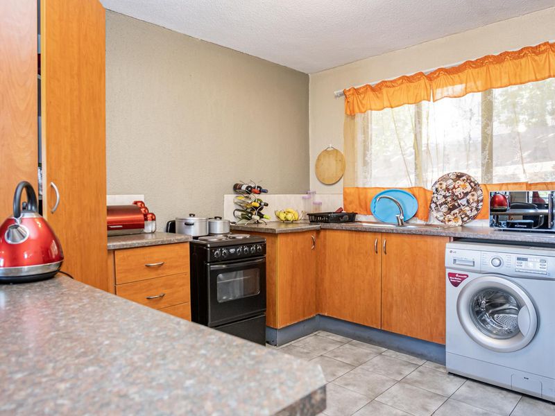 A functional kitchen featuring wood-look cabinetry, laminate countertops, a freestanding stove, and a dedicated space for a washing machine with tiled flooring.