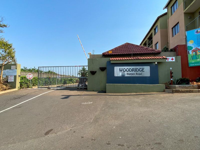 The entrance to Woodridge complex on Blamey Road, featuring a secure gated access point and perimeter fencing.