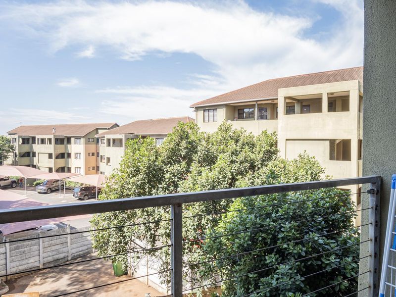 A balcony view overlooking the apartment complex grounds, featuring a metal railing and cable balustrade.
