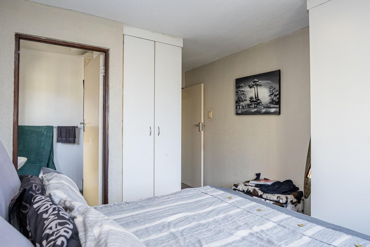 A functional bedroom featuring built-in cupboards and direct access to an adjoining bathroom, offering a practical layout with neutral finishes.
