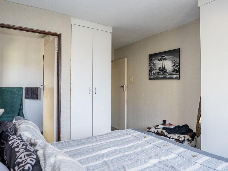 A functional bedroom featuring built-in cupboards and direct access to an adjoining bathroom, offering a practical layout with neutral finishes.