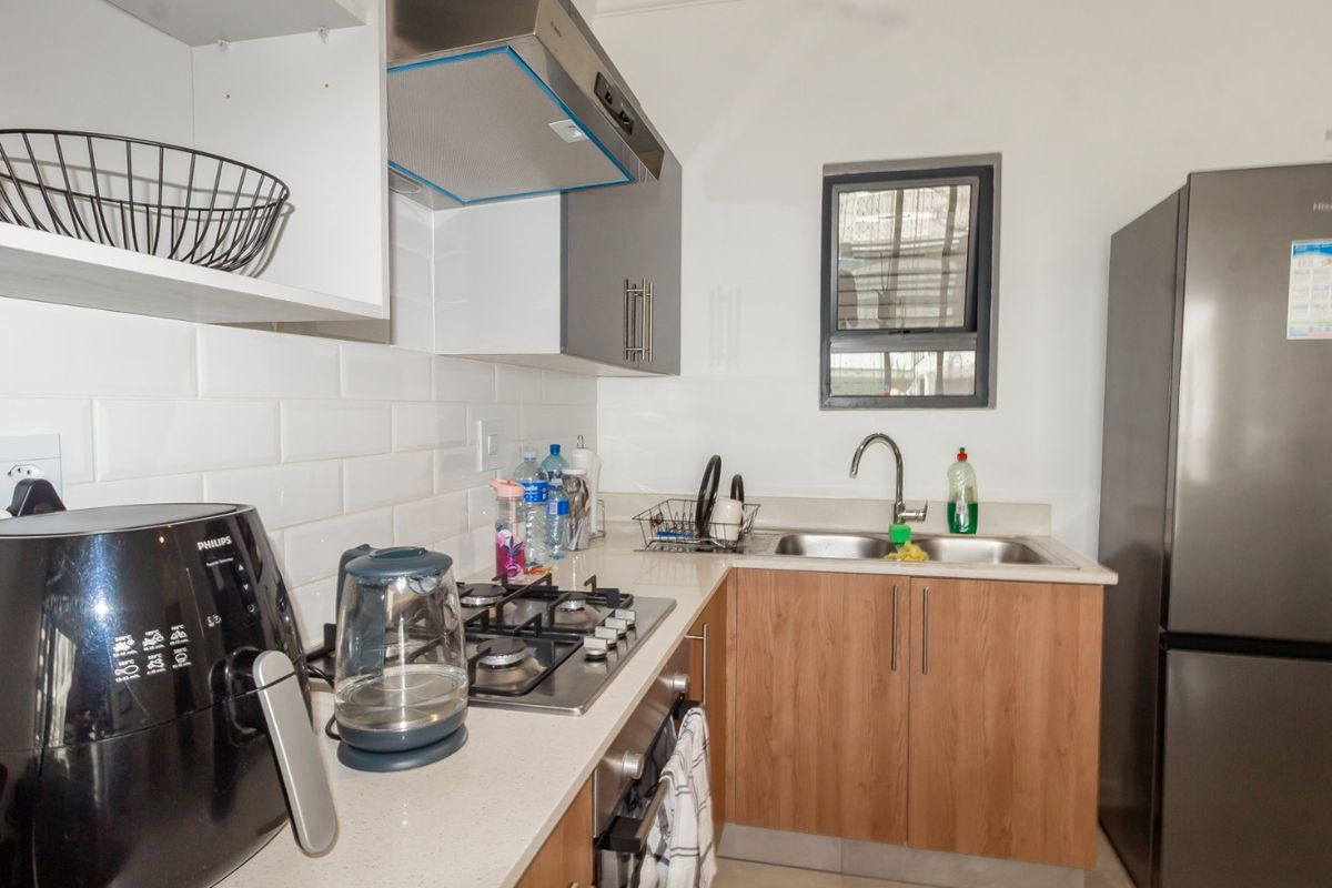 Compact kitchen featuring a gas hob, extractor fan, built-in oven, double sink, and modern subway tile backsplash with wood-finish cabinetry.