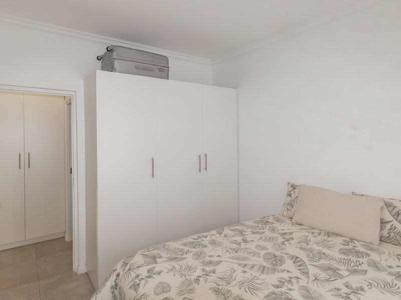 A clean and bright bedroom featuring neutral tiled flooring, coving, and a functional built-in wardrobe providing ample storage space.