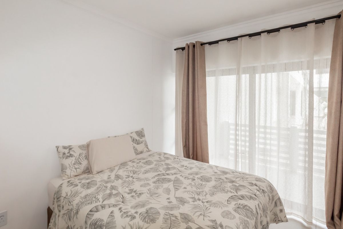 A bright bedroom featuring neutral walls, a sliding glass door with curtains, and access to an outdoor area.