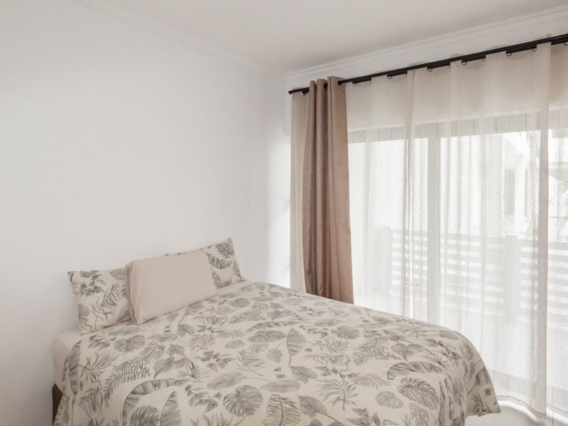A bright bedroom featuring neutral walls, a sliding glass door with curtains, and access to an outdoor area.