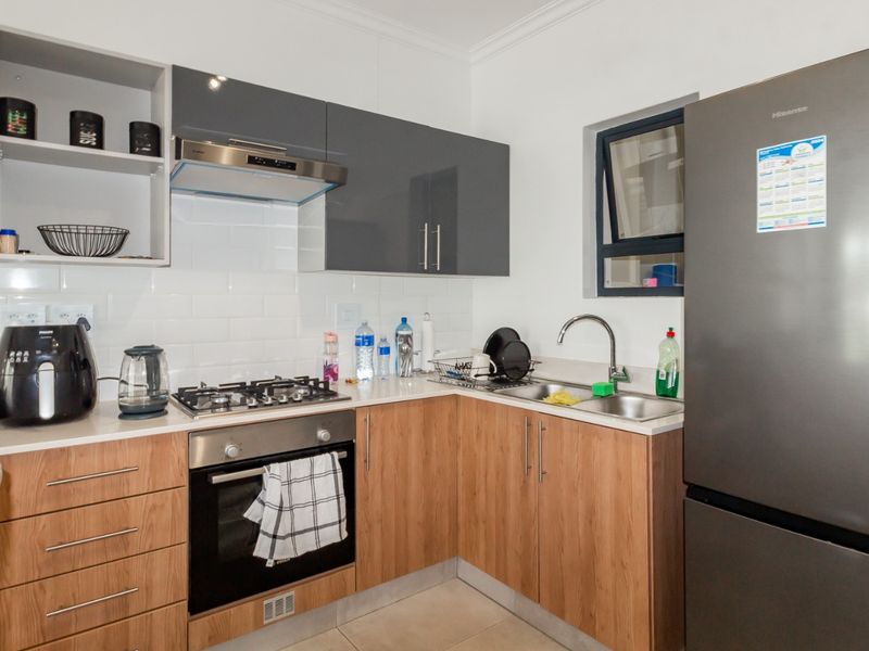 Modern kitchen featuring wood-finish cabinetry, stone countertops, subway tile backsplash, and integrated stainless steel appliances including a gas hob and oven.