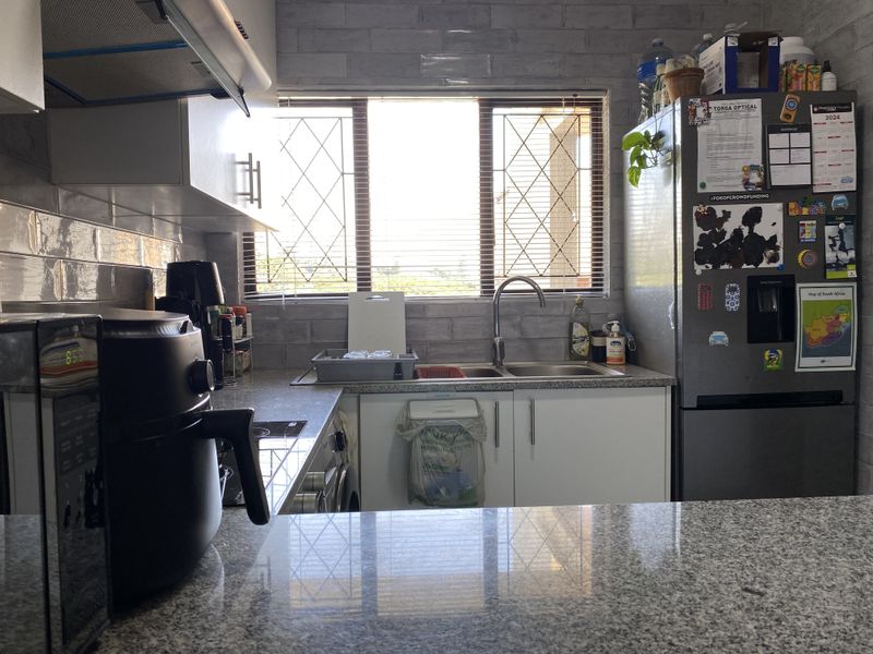 A functional kitchen featuring granite countertops, subway tile backsplash, stainless steel sink, and built-in cabinetry with an integrated extractor fan.