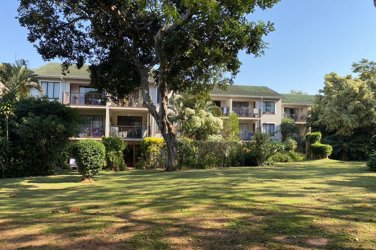 A view of the rear elevation of the apartment complex, featuring private balconies and a well-maintained, spacious communal garden with mature trees.