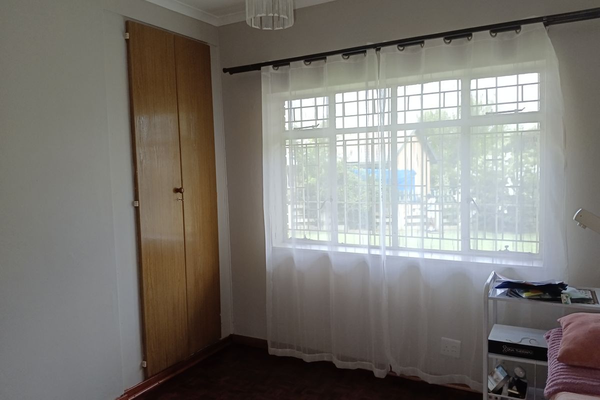 A bedroom featuring parquet flooring, a built-in wooden cupboard, and a window fitted with security bars.
