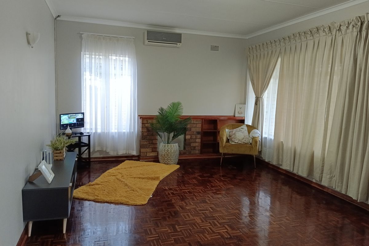 Spacious living room featuring polished parquet flooring, a classic brick fireplace with built-in shelving, and a wall-mounted air conditioning unit.