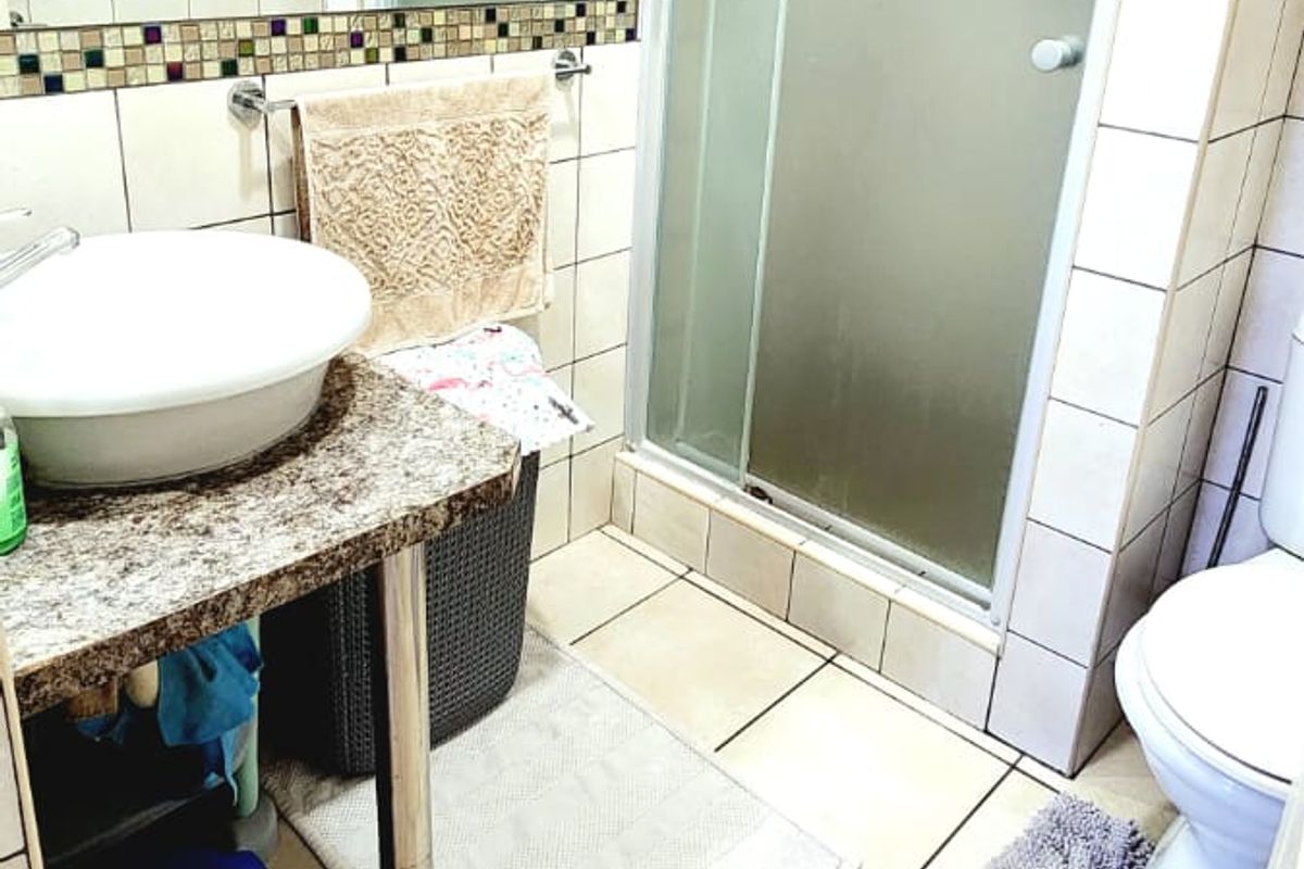 A functional bathroom featuring a vessel sink on a granite vanity, a glass shower enclosure, and neutral wall and floor tiling.